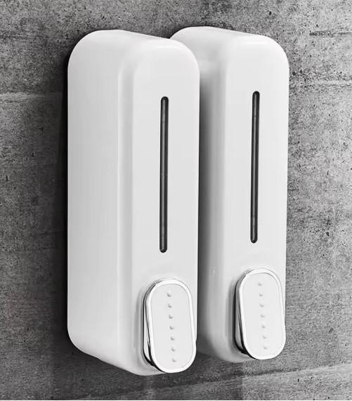 White dual wall mounted soap dispenser with transparent window and push button on gray concrete wall